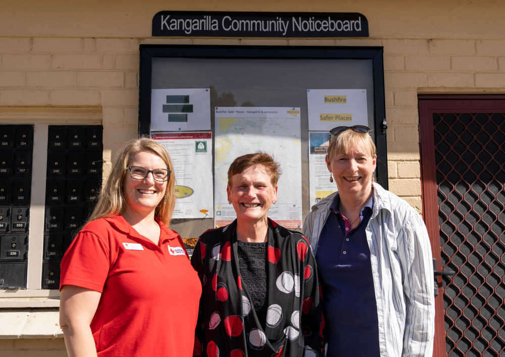 Three women standing in front of a community noticeboard