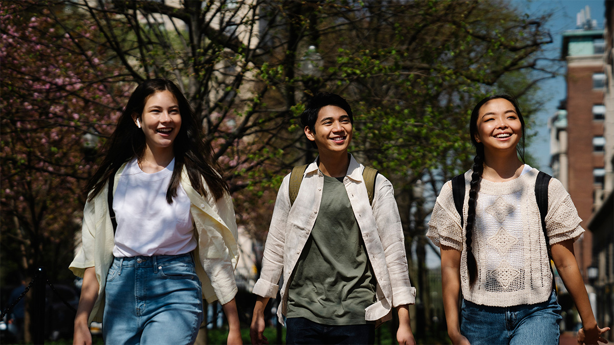 Three smiling young people walking through a park
